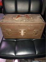 Closed old metal fishing tackle box with handle on top, showing rusty and aged condition