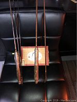 Two vintage fly rods with worn cork handles placed vertically on black chair.