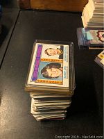 Stack of Topps hockey cards on a black surface, top card showing 1973-74 Assist Leaders featuring Bobby Orr and Dennis Hextall.