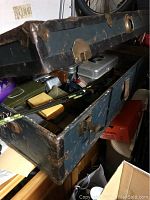 Old blue wooden fishing trunk open showing vintage fishing rods, tackle boxes, and accessories inside.