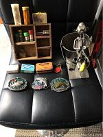 Full lot of fishing collectibles including wooden shelf with compartments, fishing belt buckles, assorted tins and boxes, and metal fisherman storage bucket with fishing figurine.
