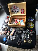 Photo of laid out wooden chest open, showing badges, pins, and various styled key chains on black surface.