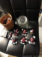 Six California Raisins figurines laid out on a black surface next to a woven basket and glass jar