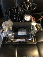 Front view showing compressor housing, gauge, coiled hose and clamps