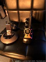 Photo showing three Motorola walkie talkies on a charging dock and a JBL iPod docking station with iPod on a black leather chair, in working order as indicated by red charging lights.