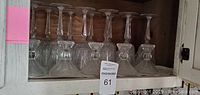 12 full lead Yugoslavian crystal glasses with long stems and starburst and diamond cut patterns, arranged on wood shelf