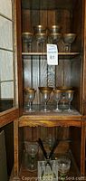 Seven glasses with wide gold rims on top shelves, four visible below on one shelf with dark wooden cabinet background