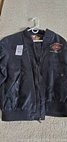 Full front view of the black nylon Harley-Davidson jacket on a hanger showing the overall condition and style.