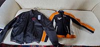 Two Ducati racing jackets laid out on a couch, showing black men's jacket and black, orange, and white women's jacket.