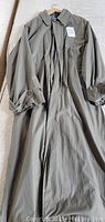 Full length men's trench coat in forest green hanging on a hanger showing front and button cuffs