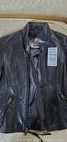 Front photo of black Harley Davidson women's leather jacket size XS, zipped open showing texture and zipper details.