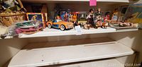 Shelf with various vintage dolls, a toy car, miniature animals, and other collectibles arranged together.