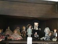 Wide shot of all collectible dolls arranged on a shelf, showing variety of sizes, clothing, and materials
