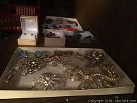 Boxes filled with an assortment of vintage costume jewelry including brooches, bead necklaces, rings, and earrings.