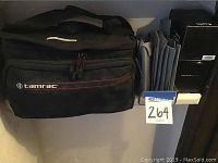 Black Tamrac camera bag and gray accessory pouches on a shelf