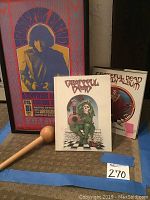 Framed Grateful Dead concert poster with two Grateful Dead books in front and wooden mallet on left.