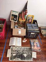 Two boxes filled with vintage magazines and books, a small vintage American flag, and a gelatin silver photograph laid out on the floor.