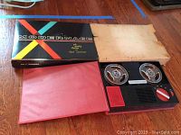 Photo of vintage Modernage portable reel to reel tape recorder with two reels and control dial in original box on wooden floor.