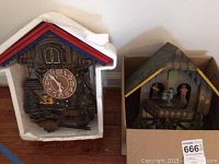 Pair of cuckoo clocks side by side, one wooden marked Rhapsodie, the other modern plastic inside box