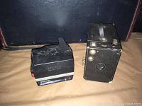 Kodak Brownie box camera and Polaroid Sun 600 land camera side by side on tabletop