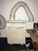 Full view of off-white Amana portable air conditioner with attached flexible vent hose, front air vents, and control panel.