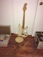Vintage Sango electric guitar with small drum and three drumsticks placed on floor against white wall