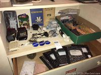 Wide shot showing the entire collection of desk items arranged on a white desk, including the calculators, composition notebooks in drawer, pinback buttons, writing instruments, extension cord, and cables.