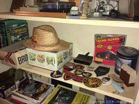 Shelf with men’s straw hat, assortment of embroidered military patches, boxed household items, and miscellaneous objects