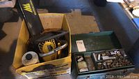 Wide view showing the cardboard box with the Eager Beaver hedge cutter and the green metal toolbox with assorted small tools and hardware.