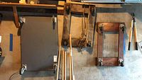 Three dolly carts hanging on a wall: one large flat metal dolly with caster wheels and two smaller wooden dollies with carpeted buffers.