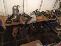 Wide shot of workbench with Stanley belt sander, hand planes, stapler, and edge trimmer items arranged with some additional tools and materials in background.