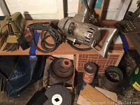 Photo showing heavy duty drill, circular blades and abrasives on wooden surface along with bolt clipper and original box.