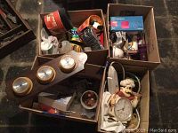 Overview of boxes containing barometer panel, chef clock, light bulbs, and other items on floor.