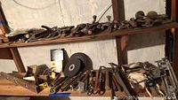 Two full shelves of assorted vintage and antique hand tools including planes, saws, wrenches, mallets, grinding wheels, and clamps.