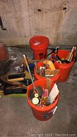 Four orange jumbo buckets containing assorted painting brushes and tools, some new rollers visible, various hand tools.