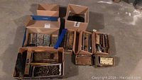 Overview of nine boxes containing assorted vintage door hardware including hinges, bolts, locks, and screws.