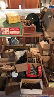 Overall view of table with multiple boxes containing vintage hardware pieces such as hinges, pulleys, screws, door card holders, and knobs.