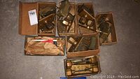 Eight small cardboard boxes on concrete floor each containing brass door knob sets with backplates and latch hardware