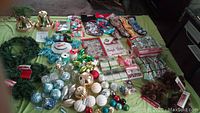 Overview of assorted Christmas decor items including bells, ball ornaments, stockings, wreaths, pine cones, and Christmas light boxes arranged on a green cloth.