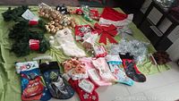 Full view of assorted Christmas decorations arranged on a surface including stockings, ornaments, garlands, lights and bows.