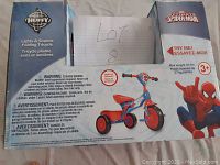 Front of box showing Marvel Spider-Man themed folding tricycle with lighting and sound features, loading window with tricycle image, and product warnings.