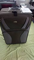 Front view of smaller El Dorado black and gray soft suitcase on green surface with a tag