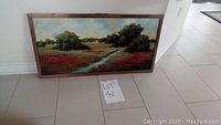 Framed nature landscape painting leaning against a wall on a tile floor, showing overall condition and frame