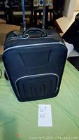 Front view of black soft-sided suitcase showing zipper pocket and top carrying handle.