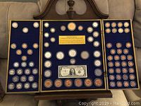 Full display of the three-panel coin set mounted on blue felt with various U.S. coins and a replica dollar bill