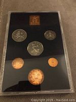 Display case showing reverse sides of 7 proof coins from 1976 set including lions, crowns, and other British emblems.