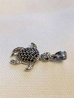 Close-up photo of front side of silver turtle pendant showing black stones on shell against white fabric background.