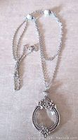 Full view of the silver tone chain with magnifying glass pendant laid flat, showing clasp and imitation pearls on chain.