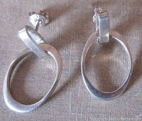 Front view showing the pair of uniquely shaped sterling silver dangling earrings, with open oval form and stud backs.