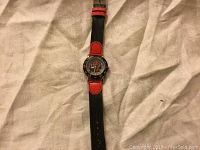 Full view of the Spider-Man watch showing black and red strap laid flat on fabric